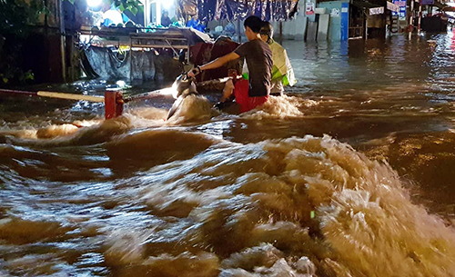 Một xe máy bị dòng nước cuồn cuộn cuốn trôi trên đường Bùi Văn Hòa. Ảnh: Phước Tuấn.
